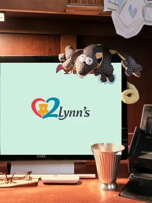 Handmade gecko draped over a computer showing the 2 Lynn's logo